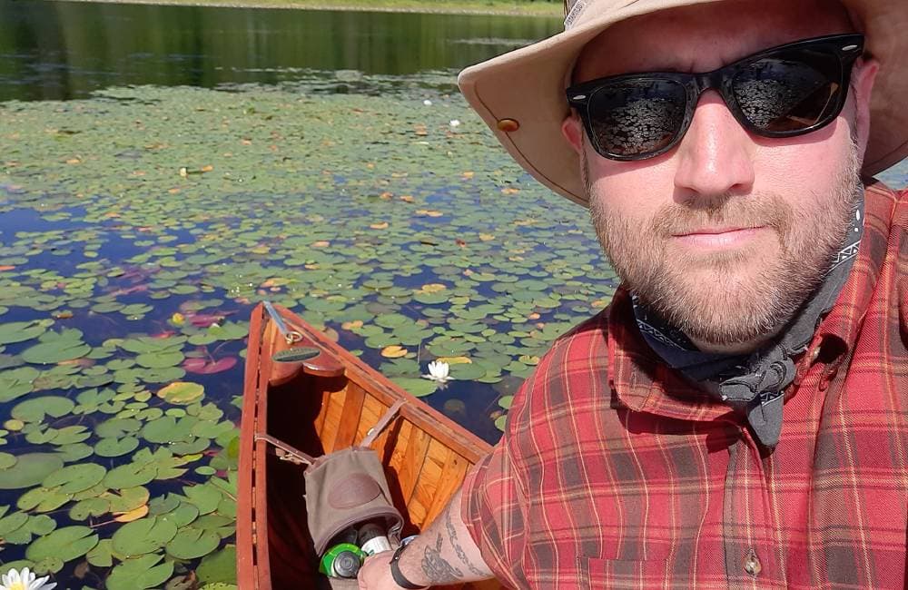 Man in sunglasses in a canoe on a lake with lillypads