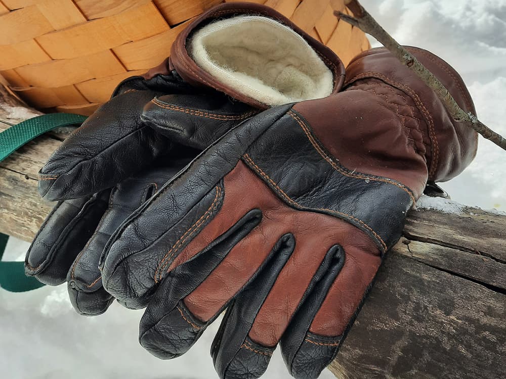 Brown and black leather Hestra Fält Guide Gloves on a log in the snow.