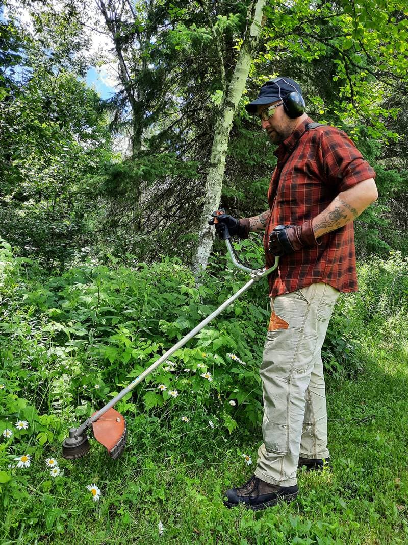 Man weed whacking wearing Hestra Fält Guide Gloves.