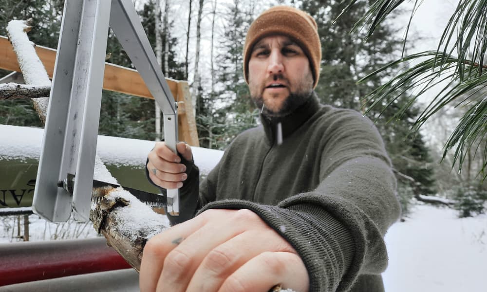 Chris cutting wood in green Woolpower full zip jacket in the snow